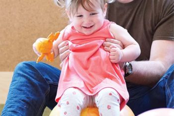 baby wearing a pink dress and sitting on a bouncy ball