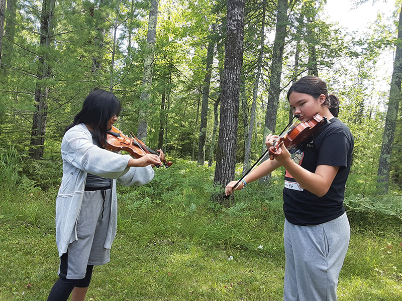 Two violin players practice at the edge of a wood