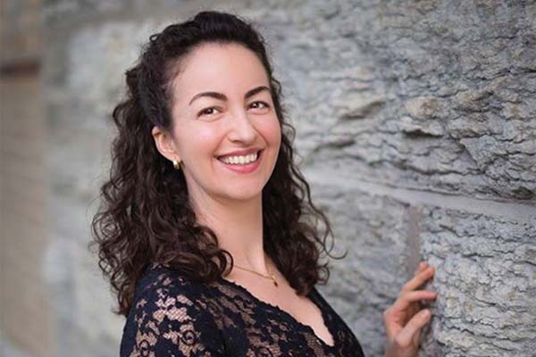 Person with long dark hair leaning against a rock wall