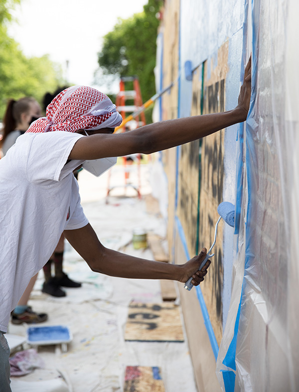 Oliver and other students painting a mural on the side of a building