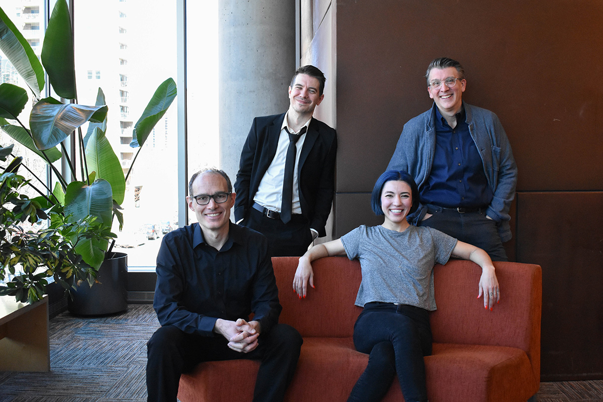 Two people sitting on an orange couch and another two people standing behind it