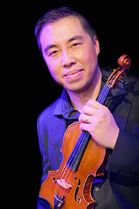 A person in front of a black background holding a violin