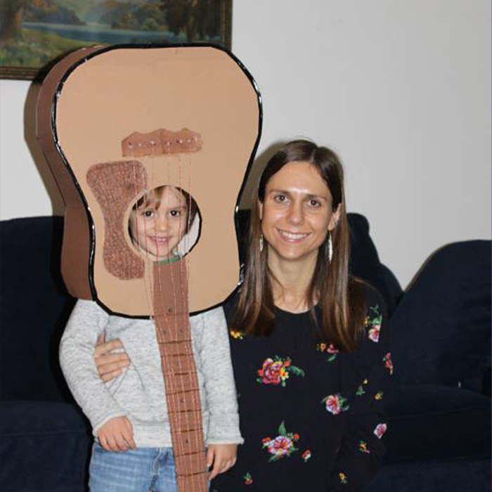 Adult with long brown hair standing by a small child with a paper guitar over their head
