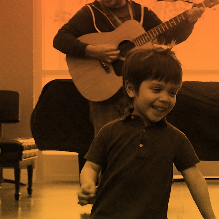 Child running around while teacher plays guitar