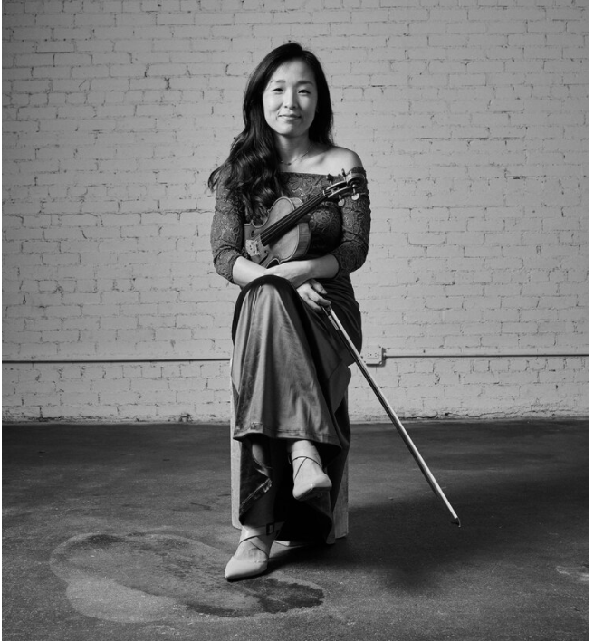 Black and white photo of a person sitting in a chair holding a violin