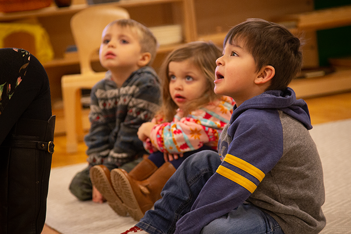 Three young children sitting on the ground looking up at something outside the photo