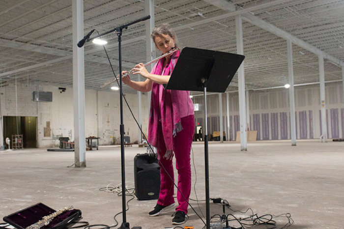 Action photo of Julie Johnson. She is wearing an all-pink outfit playing flute in front of a music stand. She has curly hair.