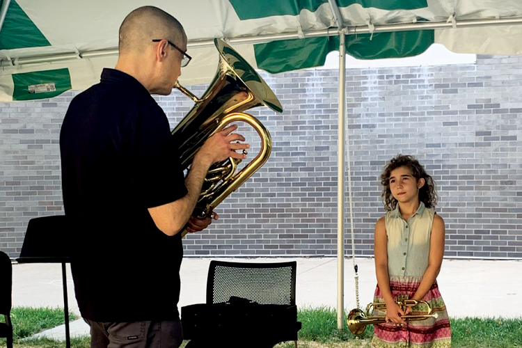 Teacher playing a tuba, young student holding a trumpet, student looking at teacher