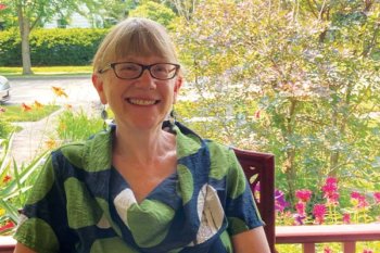 Sarah wearing a green and blue shirt sitting outside in front of plants and trees