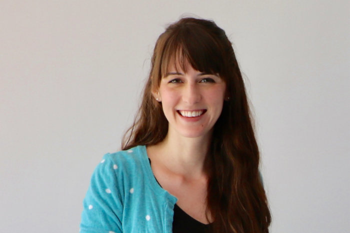 Headshot of Jessica Nagel. She has long brown hair and is wearing a blue cardigan. She is smiling.