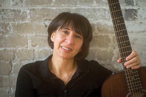 Person with short, dark hair wearing a black shirt and holding a guitar