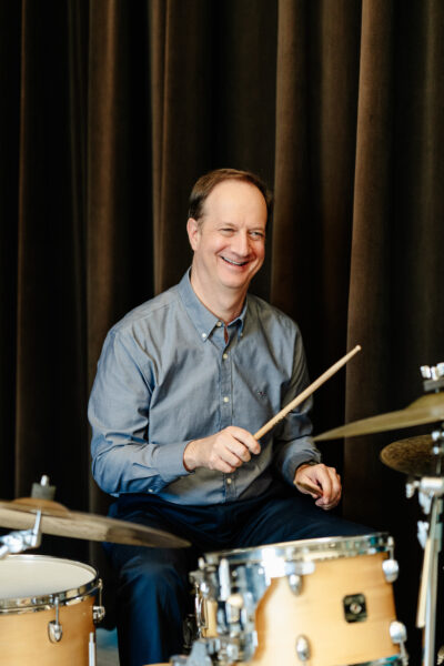 Paul Babcock sitting at a drum set with sticks in his hands. 