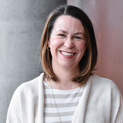 Person with medium length brown hair wearing a striped shirt and cardigan