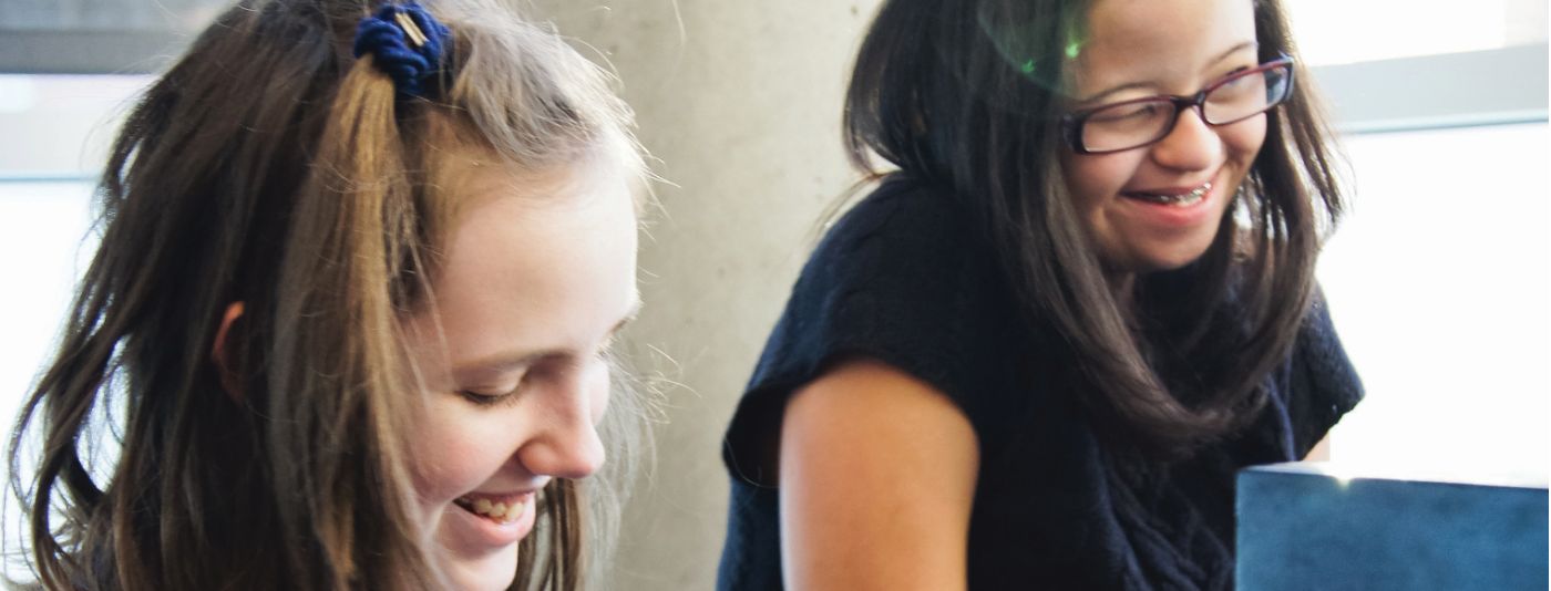 Two students sitting at a piano smiling.