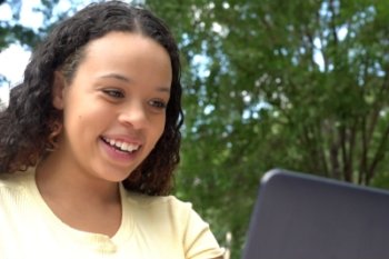 student outside smiling at laptop