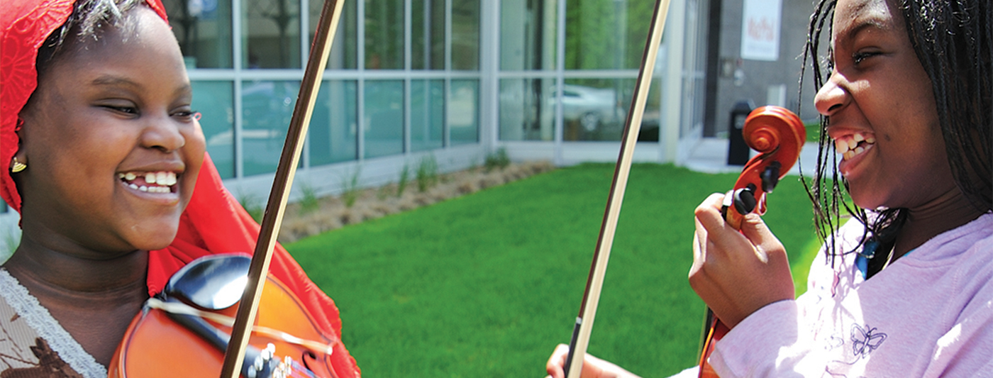 Two students holding violins and smiling