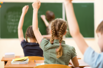 Students sitting in a classroom with their hands raised