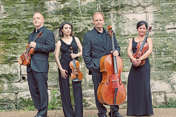 4 adults standing together. Each is holding an instrument