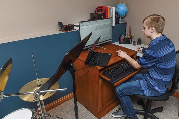 Young student wearing a blue polo shirt and jeans, sitting a desk looking at a computer.