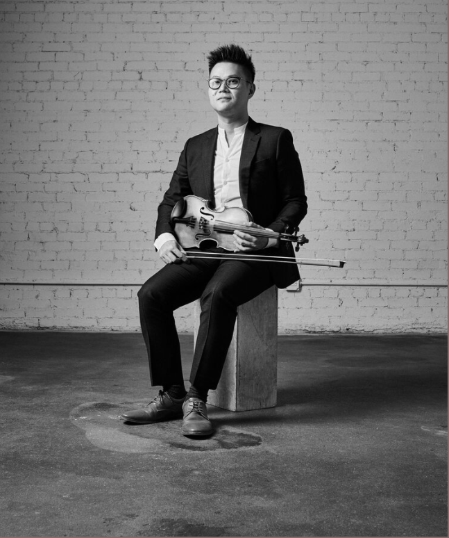 Black and white photo of a person sitting on a block and holding a violin