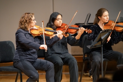 3 teachers playing violin on a stage