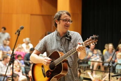 Adult performing with a guitar for a group of young students