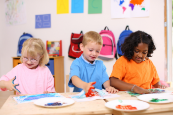 Three young children playing with finger paint