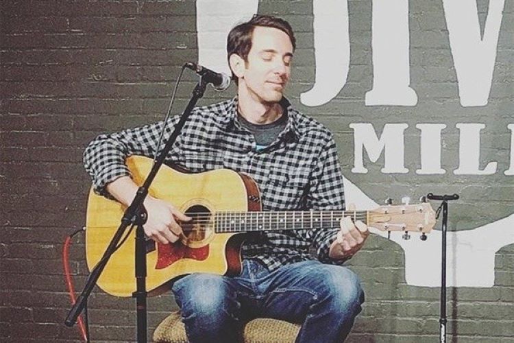 Person sitting on a stool and playing guitar into a microphone