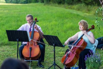 Two people playing cellos outside