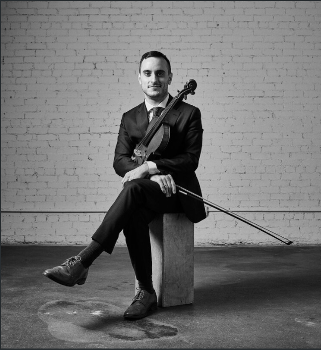 Black and white photo of a person sitting on a block holding a viola