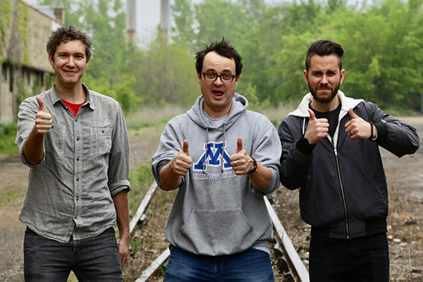 3 people standing on train tracks holding thumbs up