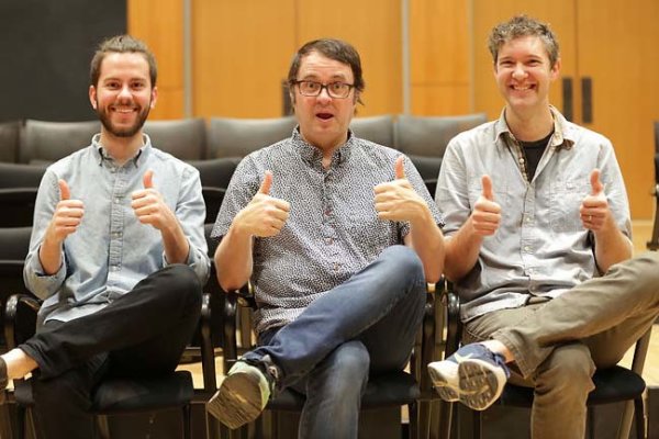 Three people sitting in chairs with the legs crossed and holding both thumbs up