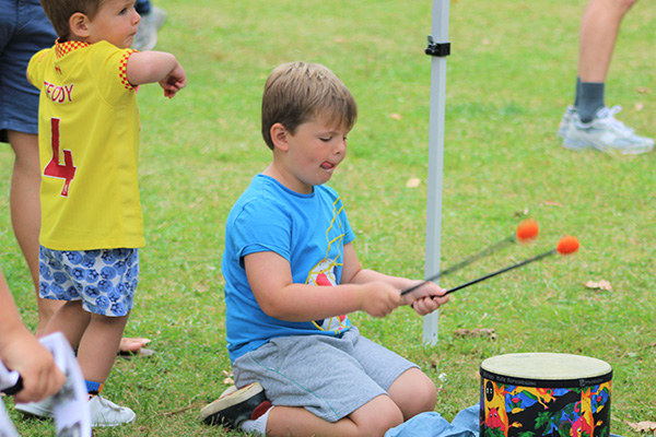 A child kneels in the grass and plays a drum