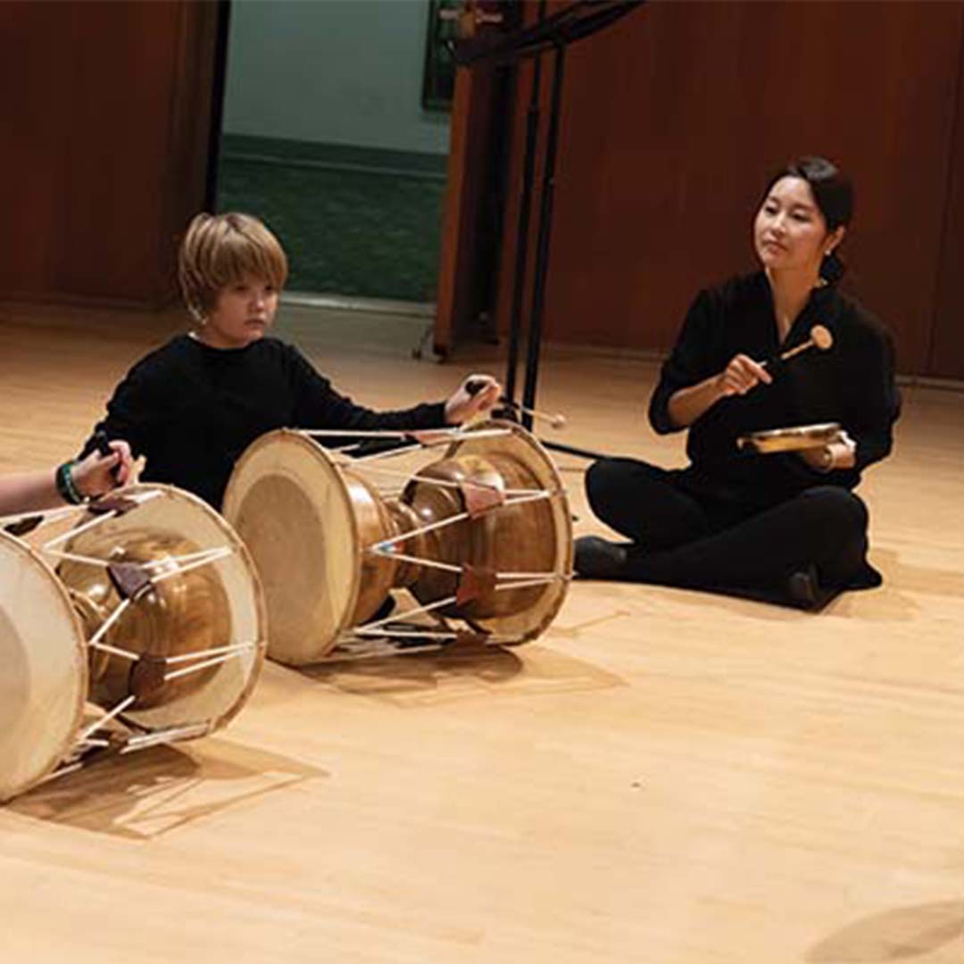 A teacher and young students playing Korean drums on stage