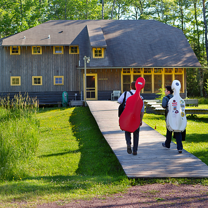 Two students carrying cellos on their back walking outside to a lodge