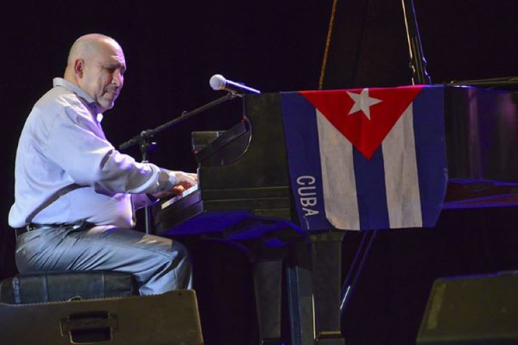 Person playing a piano. There is a cuban flag on the piano.