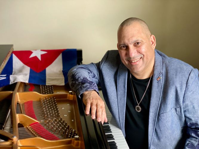 A person leaning against a piano with a cuban flag laying on it.