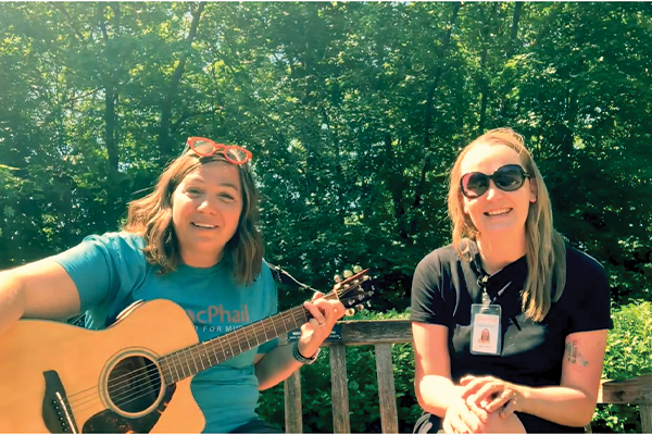 Two people sitting outside on a bench. One is playing a guitar