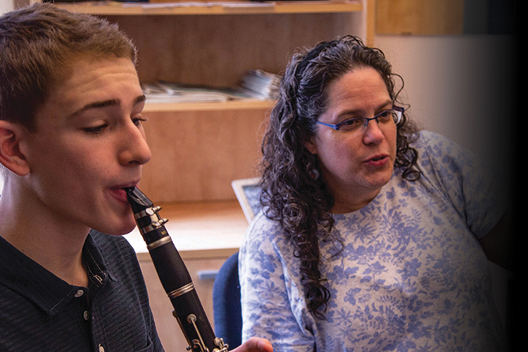 Teacher and a student sitting next to each other. The teacher is talking and the student is playing oboe.