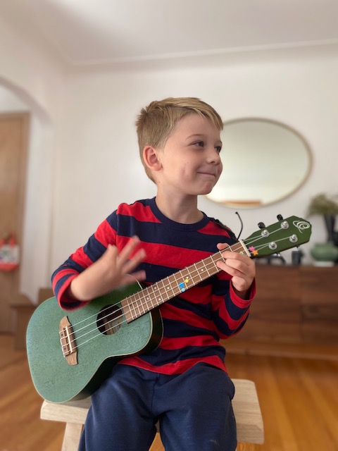 Young student wearing a striped shirt and playing a ukulele