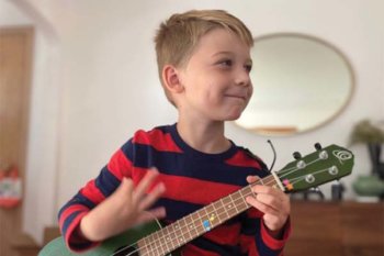 Young child wearing a striped shirt playing a ukulele