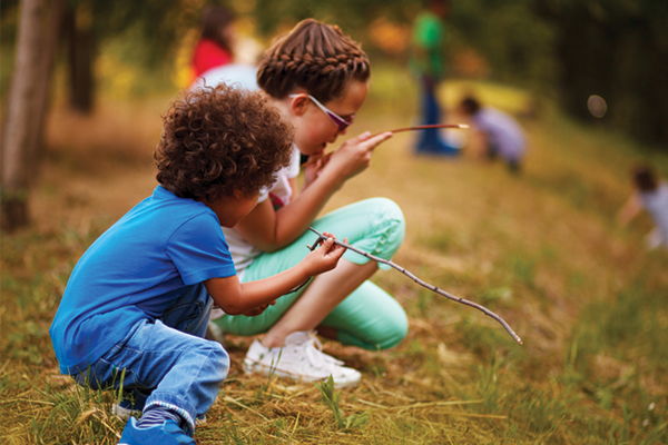 Two kids looking closely at sticks outside