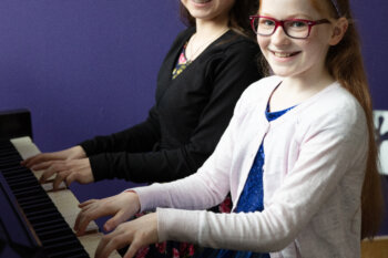 Two children playing a piano