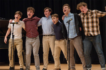 Group of students singing on stage with arms around each others shoulders