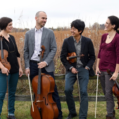 Jupiter String Quartet. Four musicians leaning on a fence in front of a corn field with their instruments.