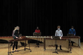 Four students playing percussion instruments on a stage