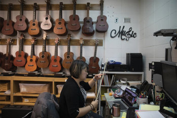 A person holding a bow in front of a computer with a wall of guitars behind them
