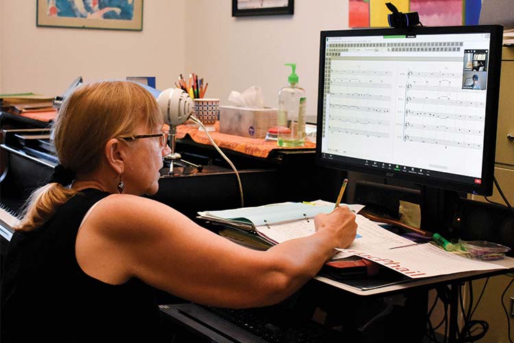 Teacher looking at music on a computer screen and writing with a pencil