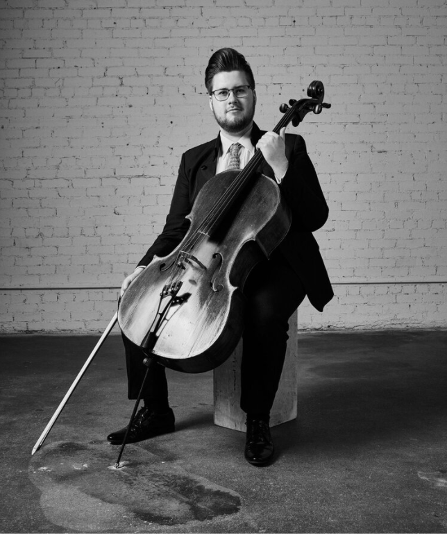 Black and white photo of a person sitting on a block with a cello.