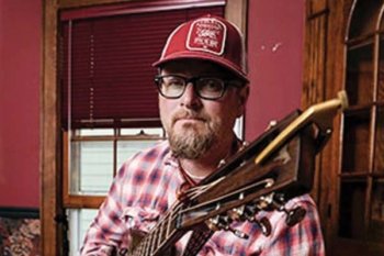 Person wearing a red hat, plaid shirt and holding a guitar